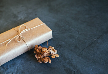 Gift box wrapped in Kraft paper with dried hydrangea flower, dried pampas grass on a dark background. New fashionable decor, copy space.
