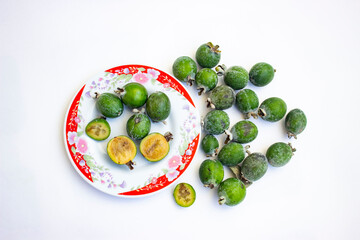 Large fleshy juicy Feijoa berries. Ripe dark green with sepals. A scattering of fruit on a light table. Whole and cut slices.