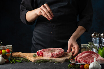 The chef in black uniform pours mustard on raw meat steak on ingredients background. Frozen motion. Backstage of preparing restaurant delicious food with spices. Concept of cooking process.