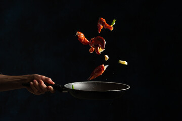 Close-up view of the chef toss up king crab legs with pieces of lime in a frying pan on dark blue background. Seafood concept. Frozen motion. Backstage of preparing traditional recipe.