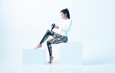 Athletic young female in sportswear massaging leg by handheld massage gun in neon light, post-workout recovery routines