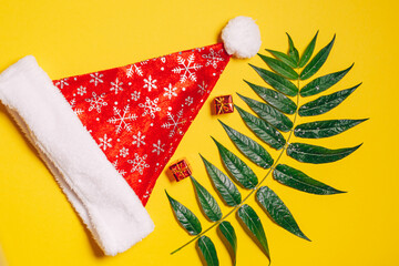 New Year and Christmas decorations. Christmas hat and Christmas toys on a yellow background with green leaves