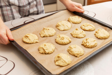 A woman holds a baking sheet with raw cookies. Home cooking.