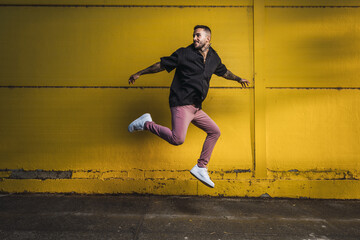 Young stylish hot man jumping next to a yellow wall