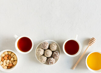 Obraz na płótnie Canvas Homemade raw candy energy balls with almond, cashews, peanut butter and hazelnuts on the plate with tea cups flat lay on gray background with copy space. Organic snack. Vegetarian food.