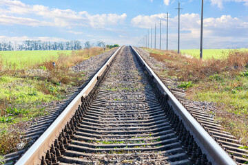 A single railway track leads up in the middle of a field against the backdrop of a rural landscape,...