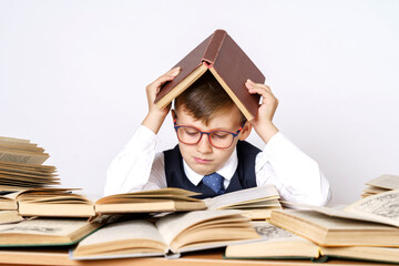 The student does his homework, reads, put the book on his head. There are many open books on the table.