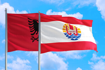 French Polynesia and Albania national flag waving in the windy deep blue sky. Diplomacy and international relations concept.
