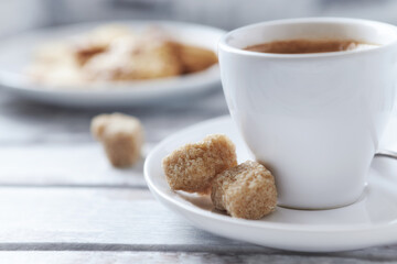 Cup of coffee and brown sugar cubes ( focus on sugar) on bright wooden background. Close up.	