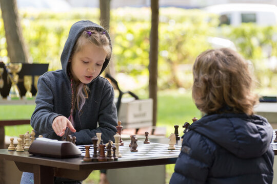 Smart Girl, Seven Years Old Is Taking Part A Kids Chess Tournament Outdoor In The Park.