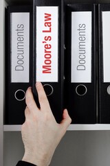 Moore's Law. File Folder is taking by a hand from office shelf. Red Text is on the label of the...