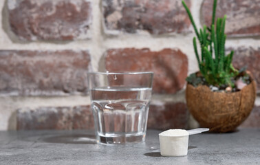 Collagen Protein Powder - Hydrolyzed, in wooden spoon on stone table, next to glass of water. Additional protein intake. Natural supplement for the beauty and health of skin, bones, joints. Close-up
