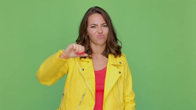 Displeased young brunette woman 20s in casual yellow leather jacket posing isolated on green background studio. People lifestyle concept. Say no with finger gesture crossed hands showing thumbs down