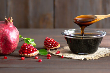 Pomegranate molasses in glass bowl, pomegranate sour sauce with fresh ripe whole and split...