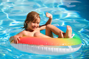 Kid in swimming pool, relax swim on inflatable ring and has fun in water on summer vacation.