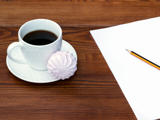 White cup of coffee and pink zefir on the wooden background. Traditional russian sweets like marshmallow. Empty A4 paper and pencil.