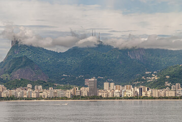 Rio de Janeiro, Brazil - December 22, 2008: Flamengo district skyline with tall buildings and forested mountains in back, one with antennas partly hidden in brown cloudscape. Guanabara bay water in fr
