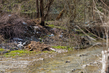A beautiful small stream is littered with a bunch of garbage, empty bottles, cellophane bags, plastic cans