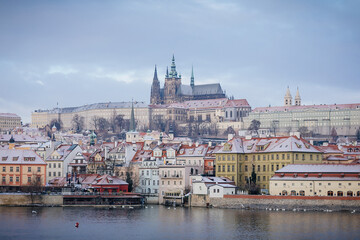Panoramic view of Prague Castle and Vltava River in winter snow lies on red tiled roofs, Picturesque landscape with Cathedral of St. Vitus and royal palace, Prague, Czech Republic