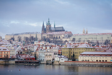 Panoramic view of Prague Castle and Vltava River in winter snow lies on red tiled roofs, Picturesque landscape with Cathedral of St. Vitus and royal palace, Prague, Czech Republic