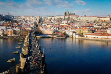 Fototapeta premium Aerial panoramic view from Old Town Bridge Tower, Karlov or Charles bridge and Vltava River in winter, sunny day, snow lies on red tiled roofs, Prague, Czech Republic