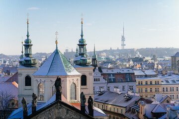 Panoramic view of Prague red tiled roofs with snow at sunny winter day, view from Old Town Bridge Tower to Clementinum and Church of the Blessed Savior, Prague, Czech Republic