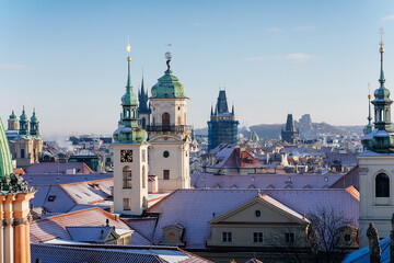 Fototapeta na wymiar Panoramic view of Prague red tiled roofs with snow at sunny winter day, view from Old Town Bridge Tower to Clementinum astronomical tower, Prague, Czech Republic