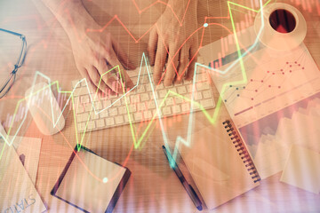 Multi exposure of man's hands typing over computer keyboard and forex graph hologram drawing. Top view. Financial markets concept.