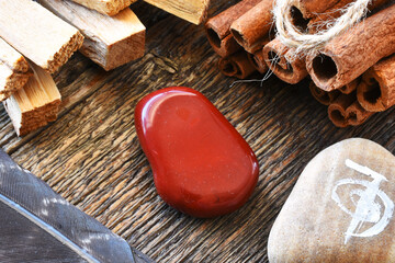 A close up image of a red jasper healing crystal with white sage and palo santo smudge sticks. 