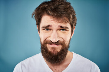 Bearded man displeased facial expression emotions close-up blue background white t-shirt
