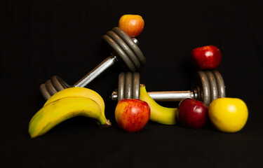 Mancuernas con frutas sobre fondo negro.