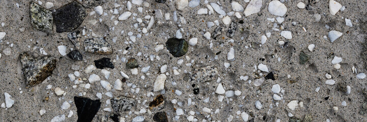 Concrete wall texture with pebbles. Decorative rough concrete surface with white, black and gray stones. Wide panoramic texture for background and design.