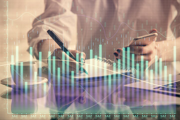 Double exposure of financial graph sketch hologram and woman holding and using a mobile device. Stock exchange concept.