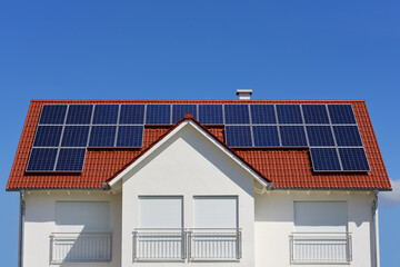 Fototapeta premium A white new house with a red tile roof and solar panels on the roof, against a blue sky, with space for text