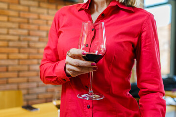 Close up on midsection of unknown woman standing and holding a glass of red wine