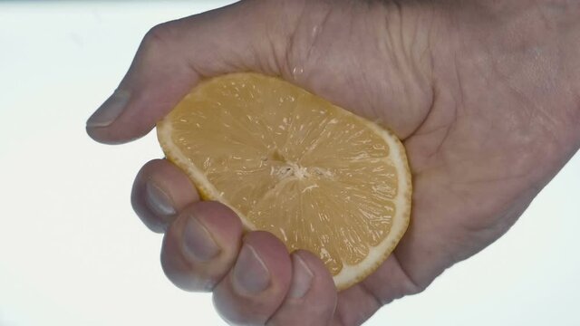 A man's hand squeezes a half of ripe yellow lemon and squeezes out drops of healthy juice, on a black background. Closeup. Slow mo, slo mo, slow motion, high speed camera