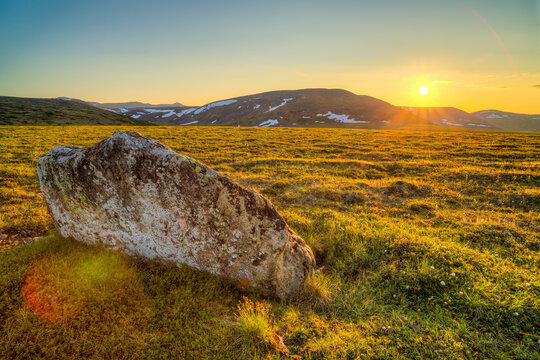 Beautiful summer Arctic landscape. Sunrise over the mountains and tundra. A large stone among the tundra in a mountain valley. Golden light from the morning sun. Chukotka, Siberia, Far East of Russia.
