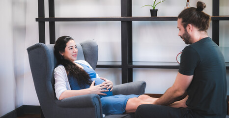 Relaxed pregnant woman sitting on chair and man massing her feet