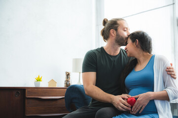 Fototapeta premium Happy pregnant couple placing baby shoes on woman big belly and spent time together while resting. Young family waiting for baby, playing with baby boots with love and passion