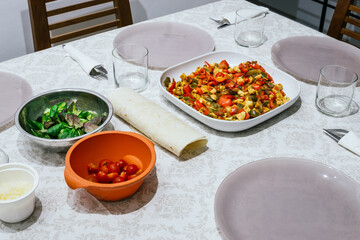 Table with homemade Mexican food. There is a plate with vegetables, corn pancakes, cheeses and salad sprouts. Everything is placed on a white tablecloth.