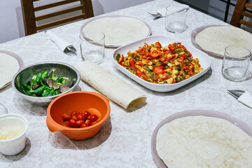 Table with homemade Mexican food. There is a plate with vegetables, corn pancakes, cheeses and salad sprouts. Everything is placed on a white tablecloth.