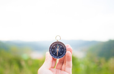 Hand holding a compass pointing to the north, with blurred mountains in the background.