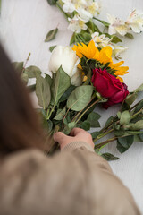 Fototapeta na wymiar person making with her hands a flower arrangement with sunflower, roses, on a white table, craft gift