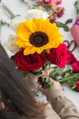 person making with her hands a flower bouquett with sunflower, roses in the background work space