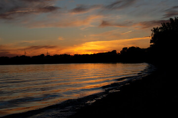 Fototapeta na wymiar Orange Sunset Reflected on Lake with Forest Silhouette 