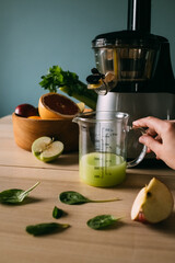 juicer, fruit and measuring cup with juice on the table. Hand holding a measuring cup