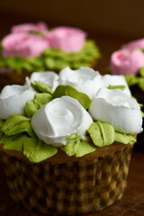 cupcake decorated with chantilly with rose design, placed on a wooden base, diffuse background of more cupcake