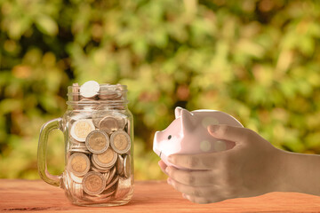 Coin money in a glass jar and a piggy bank in hand