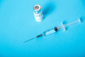 On a blue background, a syringe and a vial of coronavirus vaccine.