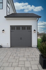 Single car classic insulated steel raised panel gray garage door framed with a gray trim to add accent, with transom light windows on a new suburban American home with stone drive way blue cloudy sky - obrazy, fototapety, plakaty